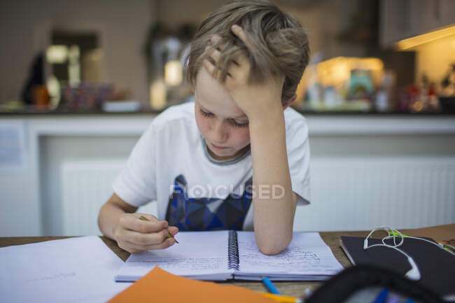 Сосредоточенный мальчик делает уроки за столом — стоковое фото
