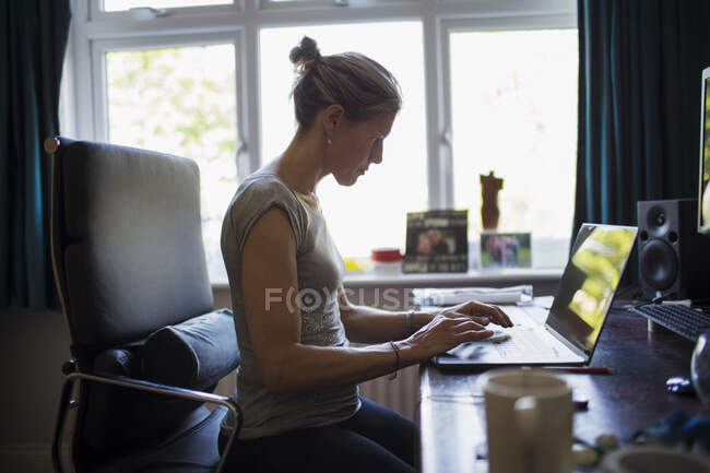Жінка працює з дому на ноутбуці в домашньому офісі — стокове фото