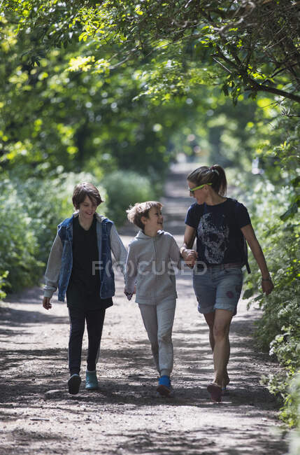 Madre e hijos caminando por el sendero del parque soleado - foto de stock