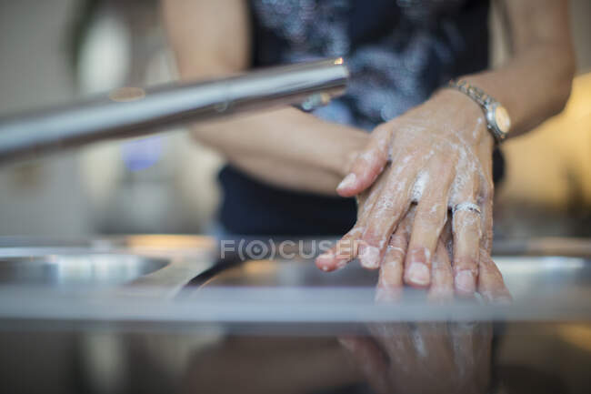 Cerca de la mujer lavándose las manos con jabón en el fregadero - foto de stock