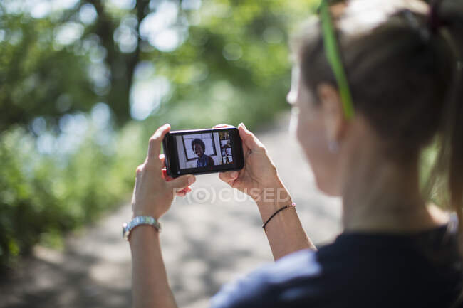 Femme chat vidéo avec des amis sur l'écran du téléphone intelligent dans un parc ensoleillé — Photo de stock