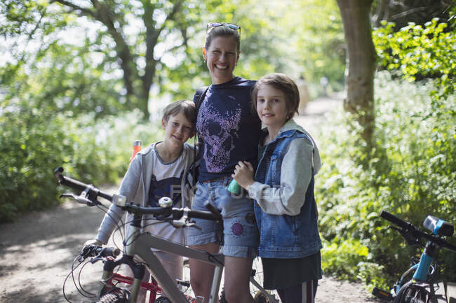 Retrato feliz madre e hijos disfrutando de paseo en bicicleta en el soleado parque - foto de stock