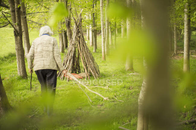 Senior woman making branch teepee in woodland — Stock Photo
