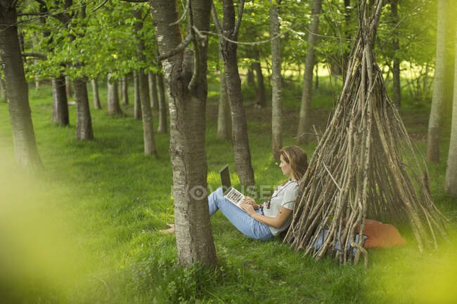 Mulher com laptop relaxante em teepee ramo na floresta — Fotografia de Stock