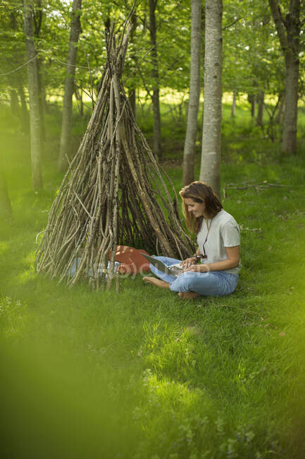 Жінка з ноутбуком розслабляється на гілці тепі в лісі — стокове фото