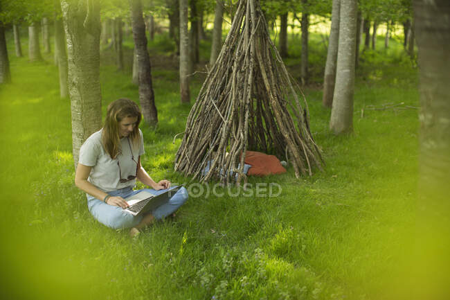 Mujer joven usando el ordenador portátil en la rama tipi en el bosque - foto de stock
