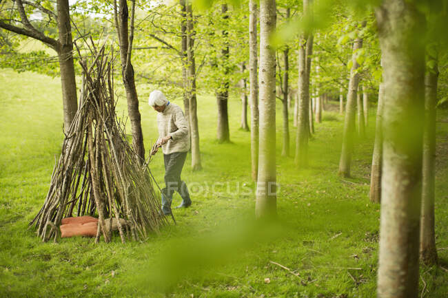 Senior woman making branch teepee in woodland — Stock Photo
