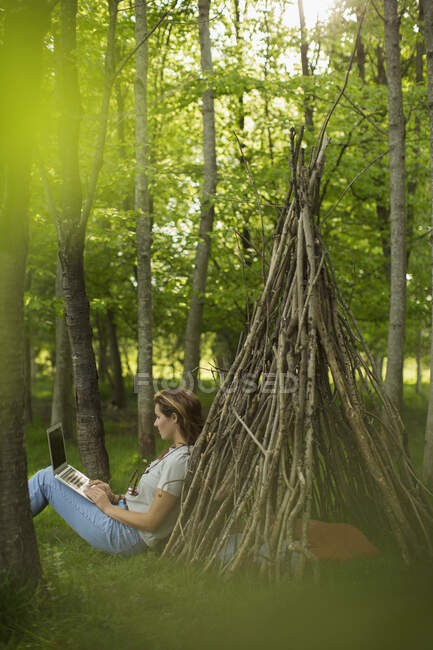 Mulher usando laptop no teepee filial na floresta — Fotografia de Stock