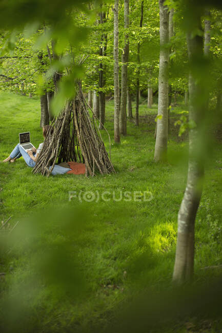 Woman using laptop at branch teepee in woodland — Stock Photo