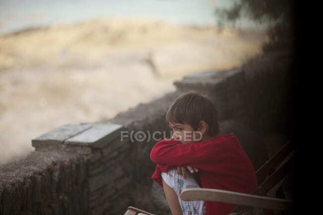 Niño pensativo sentado a lo largo de pared de roca - foto de stock