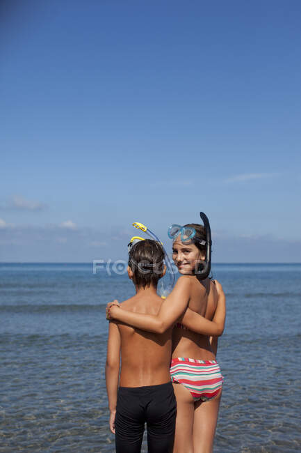 Brother and sister wearing snorkels and hugging on beach — Stock Photo