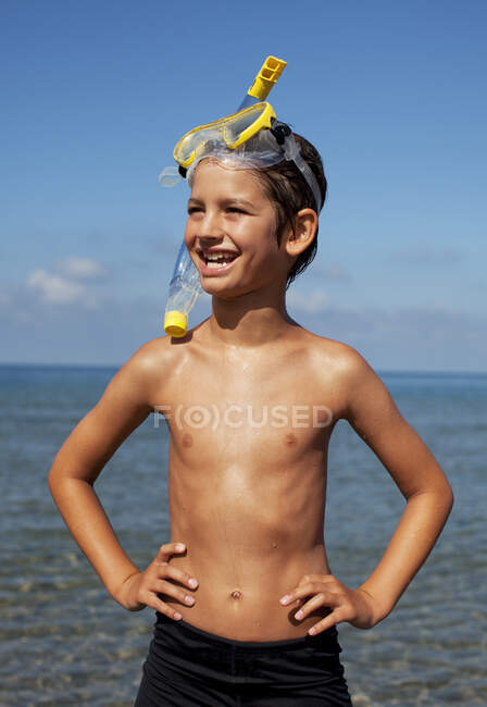 Улыбающийся мальчик в плавках и очках на пляже — стоковое фото