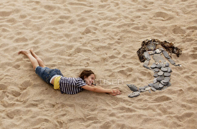Girl mimicking rock mermaid on beach — Stock Photo