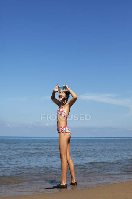 Menina sorridente vestindo óculos e nadadeiras na praia — Fotografia de Stock