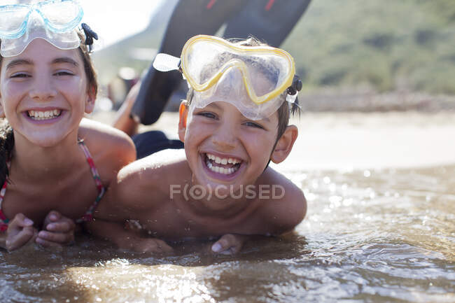 Enthusiastic brother and sister wearing goggles and laying in ocean — Stock Photo