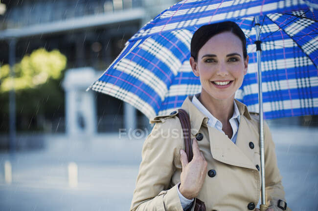 Усміхнена бізнес-леді в траншеї пальто під парасолькою — стокове фото