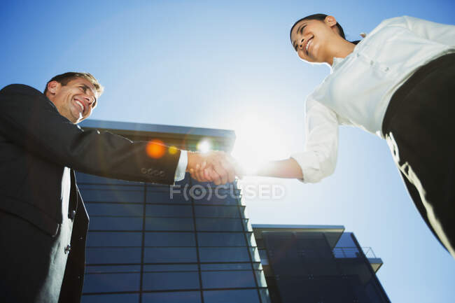 Businessman and businesswoman shaking hands below highrise — Stock Photo