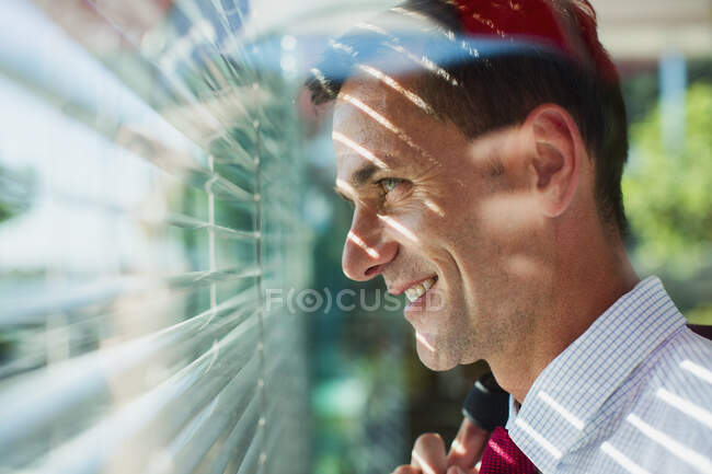 Uomo d'affari che guarda fuori dalla finestra tende — Foto stock