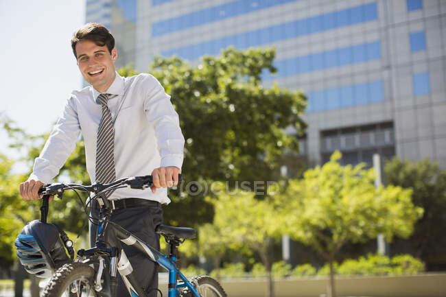 Улыбающийся бизнесмен с велосипедом на улице — стоковое фото