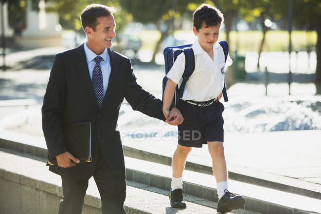 Бизнесмен и сын держатся за руки в городском парке — стоковое фото