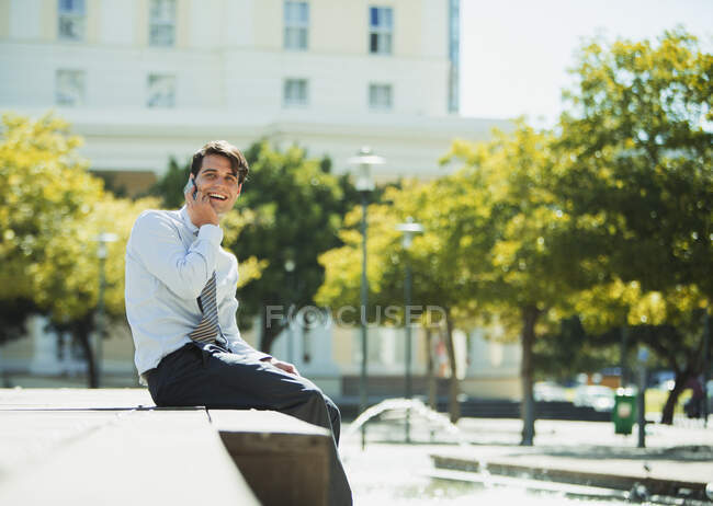 Empresário sorrindo falando no celular no parque urbano — Fotografia de Stock