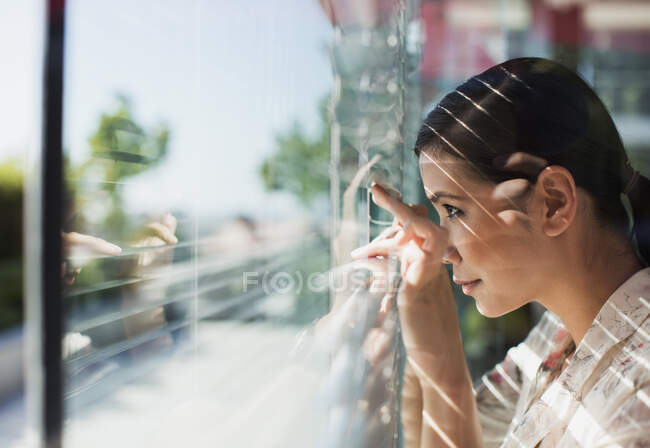 Businesswoman peering out window blinds — Stock Photo