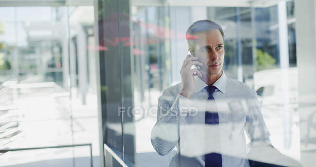 Businessman talking on cell phone at office window — Stock Photo
