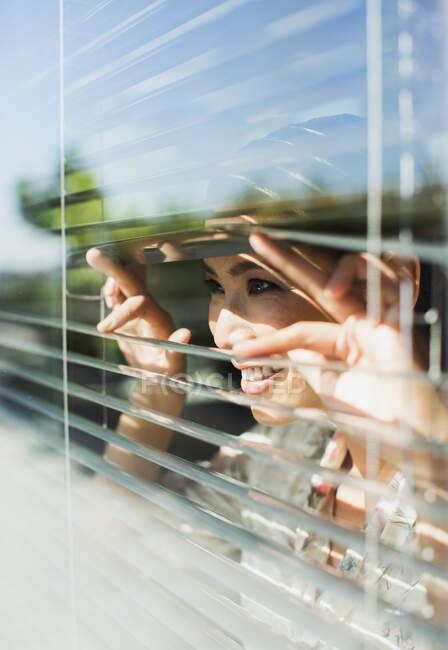 Smiling woman peering out window blinds — Stock Photo