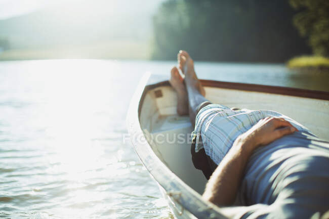 Человек лежит в лодке на спокойном озере — стоковое фото