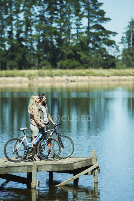 Pareja con bicicletas en el muelle con vistas al lago - foto de stock
