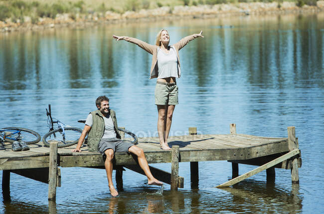 Exuberant woman with arms outstretched on dock over lake — Stock Photo