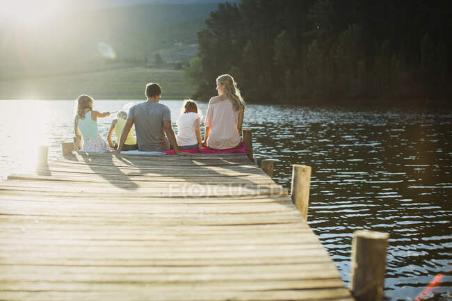 Семья сидит на краю дока над озером — стоковое фото
