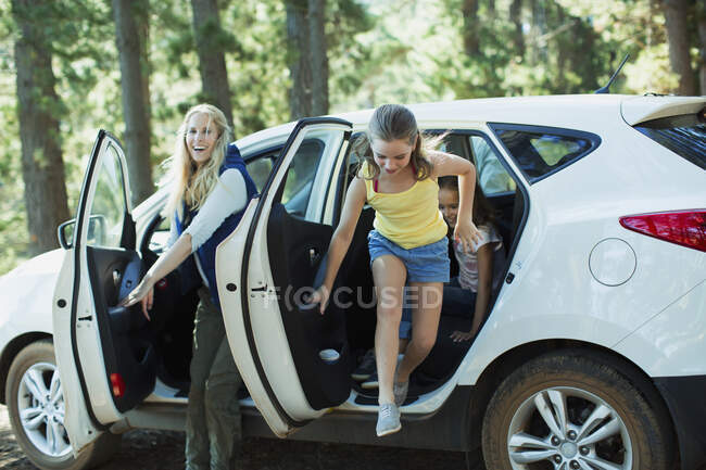 Madre e hijas bajando del coche en el bosque - foto de stock