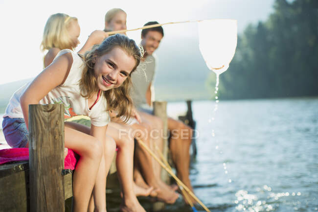 Familia sonriente con redes de pesca en el muelle sobre el lago - foto de stock