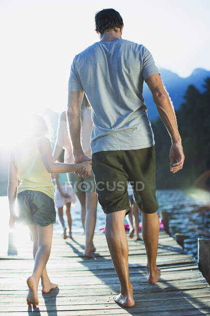 Padre e hija tomados de la mano caminando en el muelle sobre el lago - foto de stock