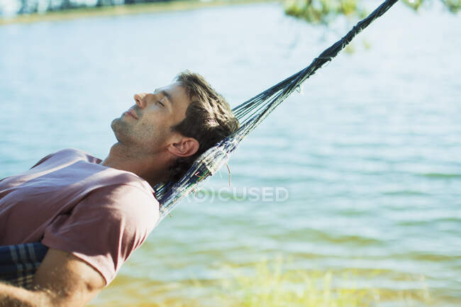 Sereno homem deitado na rede ao lado do lago — Fotografia de Stock