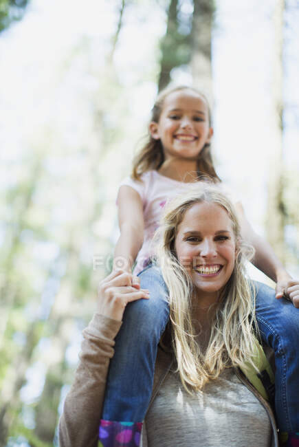 Mother carrying daughter on shoulders in woods — Stock Photo
