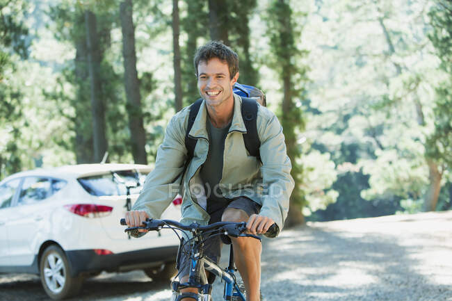 Hombre sonriente montando bicicleta de montaña en el bosque - foto de stock