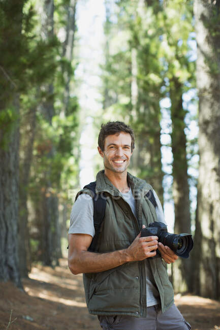 Uomo sorridente con fotocamera digitale nel bosco — Foto stock
