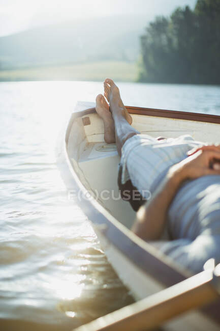 Hombre sereno yaciendo bote de remos en el lago tranquilo - foto de stock