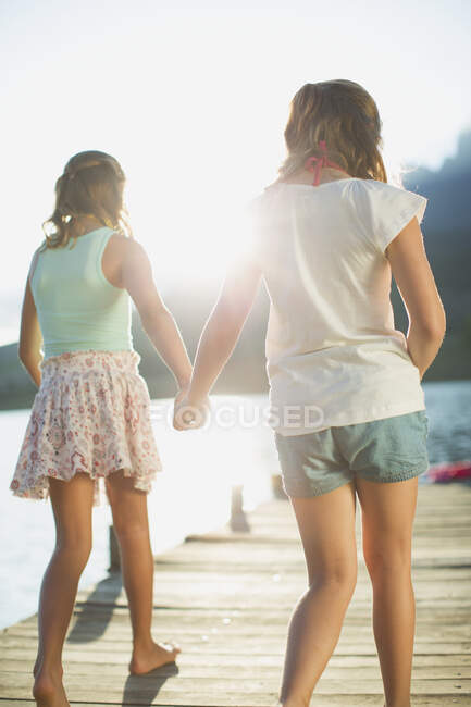 Irmãs de mãos dadas na doca sobre o lago — Fotografia de Stock