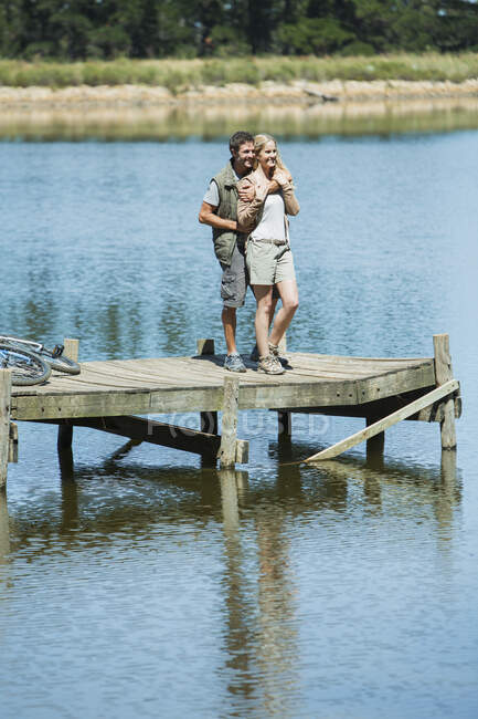 Lächelndes Paar umarmt sich auf Dock über See — Stockfoto