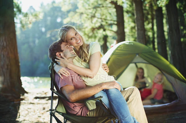 Femme souriante assise sur les genoux des maris au camping dans les bois — Photo de stock