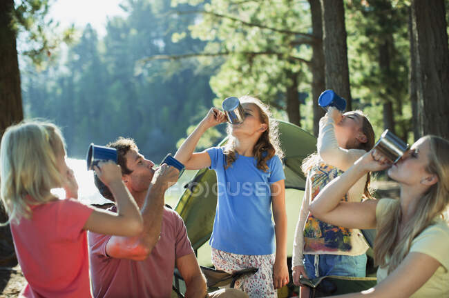 Famiglia che beve da tazze al campeggio nel bosco — Foto stock