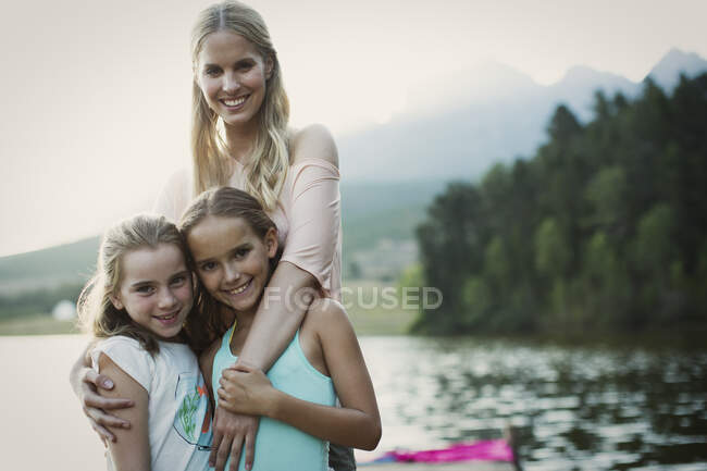Madre e hijas sonriendo al lado del lago - foto de stock