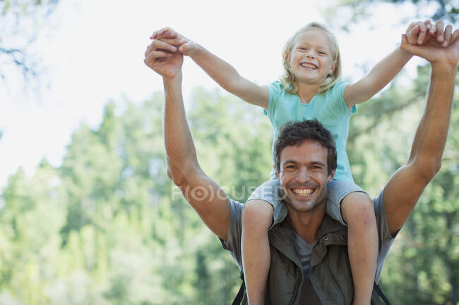 Улыбающийся отец носит дочь на плечах в лесу — стоковое фото