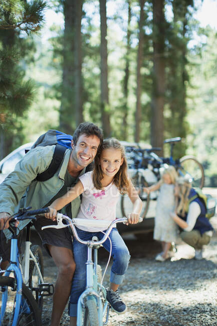 Père et fille souriants sur des vélos dans les bois — Photo de stock
