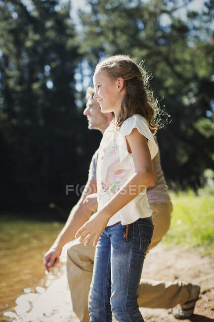 Улыбающиеся отец и дочь бросают камни на берегу озера — стоковое фото