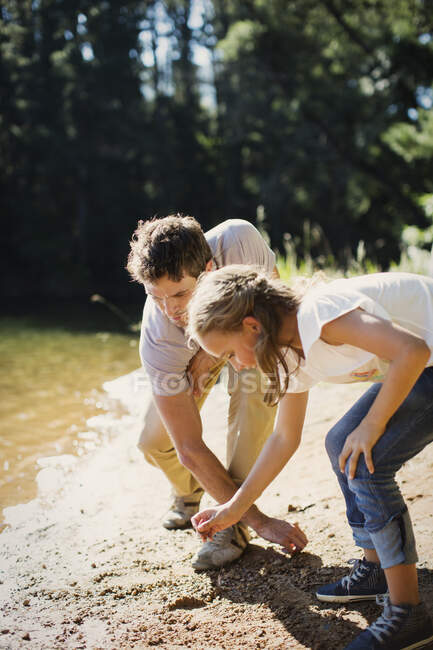 Padre e hija recogiendo piedras en la playa junto al lago - foto de stock