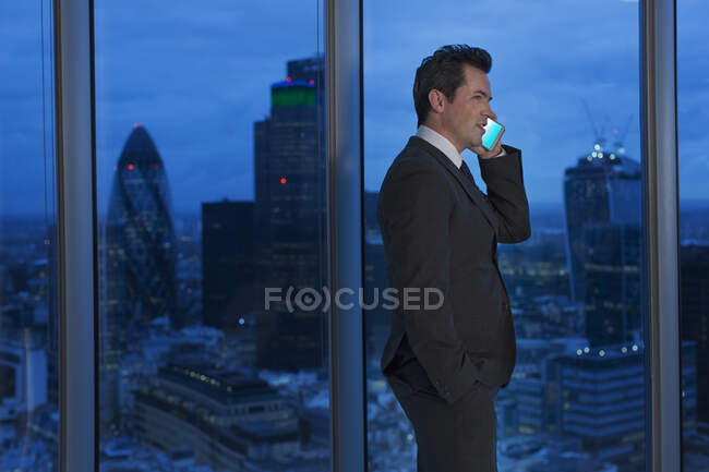 Businessman talking on cell phone in urban window at night — Stock Photo